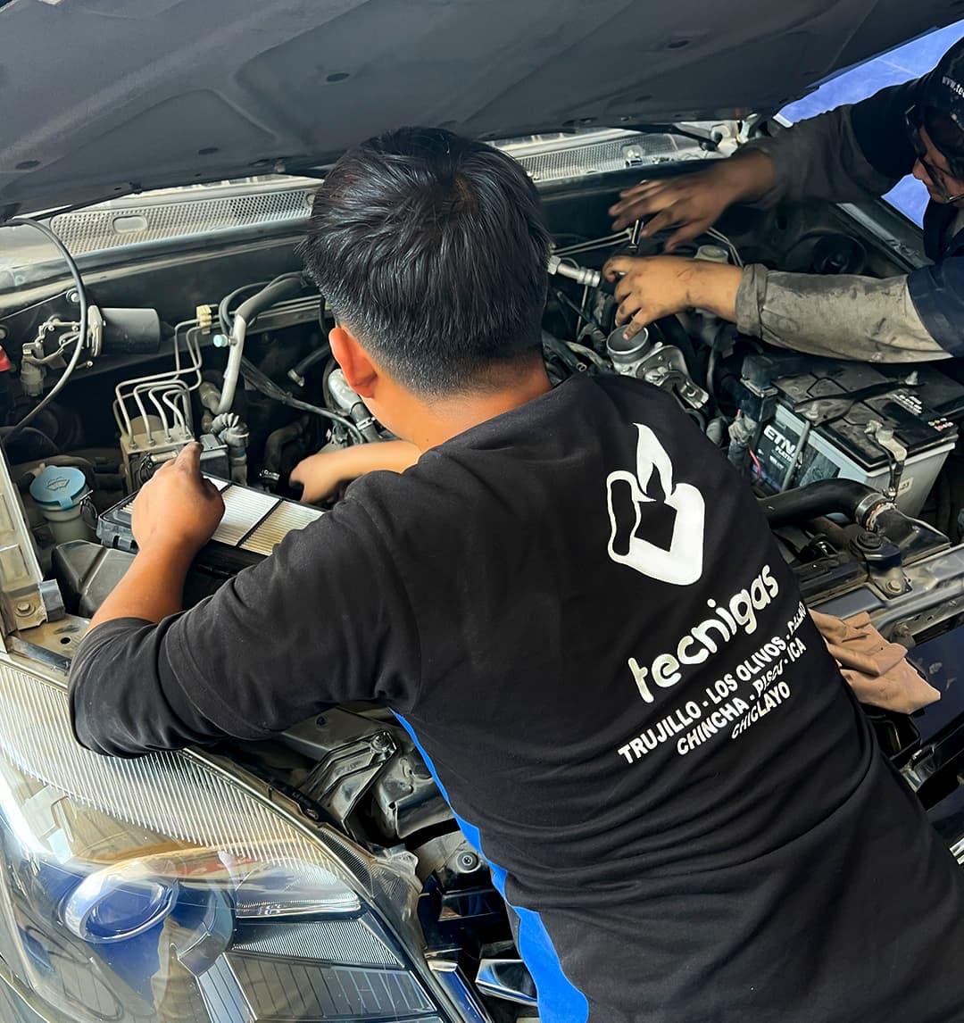 Dos técnicos de Tecnigas trabajando sobre el motor de un vehículo con el capó abierto